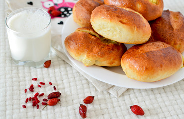 Yeast buns on ceramic plate on white table, glass of milk, rosehip berries. Pies with potatoes. Delicious breakfast, homemade food. Baking, dough.