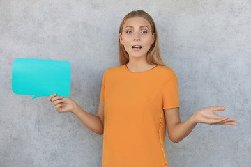 Confused young woman holding empty speech bubble isolated over grey background