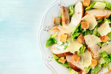 Caesar salad close-up. Slices of chicken breast, green lettuce, Parmesan cheese, and croutons, overhead shot with copy space