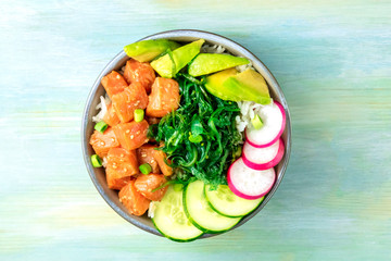 Salmon poke with avocado, wakame and cucumber, shot from above on a teal blue background with a place for text