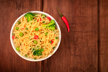 Soba noodles with broccoli and a red pepper, shot from the top on a dark rustic wooden background with a place for text