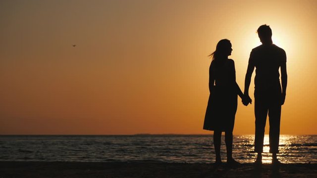 Silhouettes of a young couple in love standing near the sea at sunset