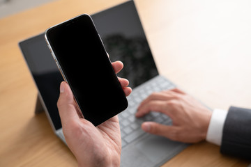 スマートフォンをみながらパソコンを使うビジネスマン