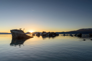 Sun setting behind Bonsai Rock, Sunset reflection in the water, Lake Tahoe, California, USA