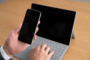 スマートフォンをみながらパソコンを使うビジネスマン