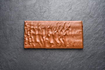 Whole milk chocolate bar on black slate background