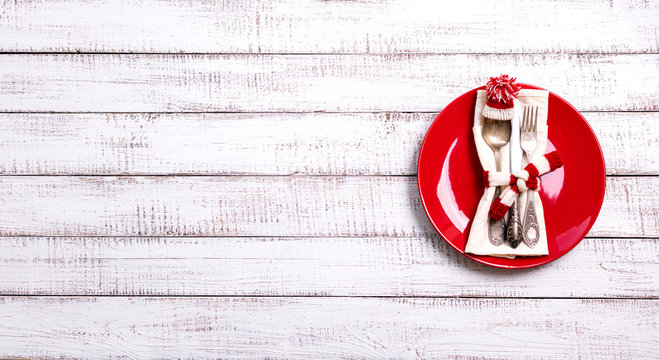 Christmas table setting with holiday decorations in the form of a knitted hat and scarf in white and red on an old wooden background with copy space.