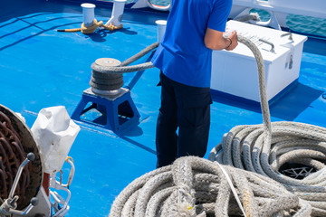 Sailor on the ship is giving mooring in the port. The rope is coiling and wounding in a spiral or sequence of ring