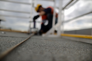 Defocused of rope access engineer inspector technician pull testing fall arrest, fall restraint roof anchor point horizontal safety line prior to used construction site Sydney, CBD, Australia   