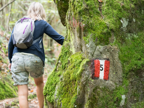 An Italian walking route indicated by a hand painted sign.Red and white stripes.A female backer in background.Image