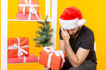 Young handsome man in a Santa Claus hat is holding congratulatory gifts next to a Christmas tree. Concept of holidays of christmas and new year.