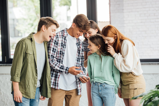 group of happy friends laughing while using smartphone
