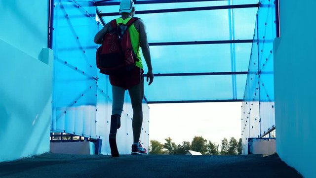 A man with a prosthetic leg is fixing a backpack while walking