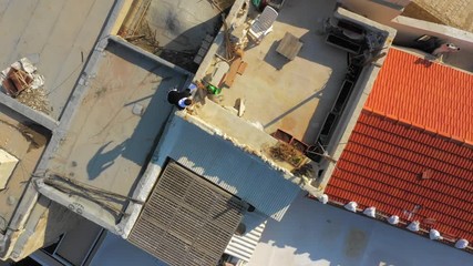 Aerial: Man Does Parkour Across Rooftops of Buildings in Tel Aviv on Sunny Day - Powered by Adobe