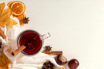 A cup of mulled wine with spices, scarf, spices, dry leaves and oranges on the table. Autumn mood, a method to keep warm in the cold, copy space.