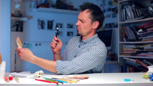 A man at a table examines a 50 euro bill through a magnifying glass