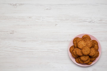 Cereal cookies on a pink plate on a white wooden surface, top view. Flat lay, overhead, from above. Copy space.