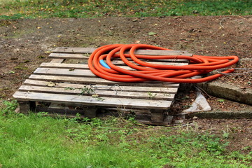 Broken wooden pallet with orange plastic hose on top surrounded with grass and fallen leaves in...