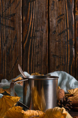 Iron mug with black coffee, spices, on a background of a scarf, dry leaves on a wooden table. Autumn mood, a warming drink. Copy space.