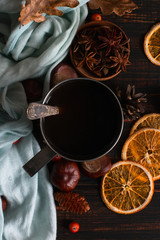 Obraz na płótnie Canvas Iron mug with black coffee, spices, dry oranges, on a background of a scarf, dry leaves on a wooden table. Autumn mood, a warming drink. Copy space.