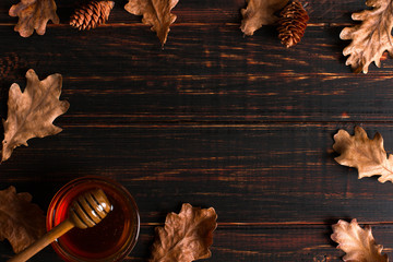 Honey flows from a stick into a jar. Rustic sweet autumn photo, wooden background and dry leaves,...