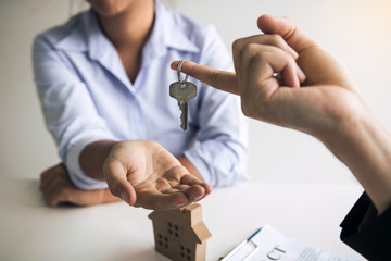 Hand of real estate agent passes the key to new homeowners in office with buyer house concept.