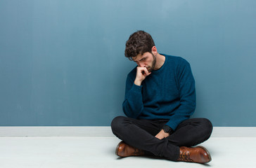 young handsome man sitting on floor feeling serious, thoughtful and concerned, staring sideways...