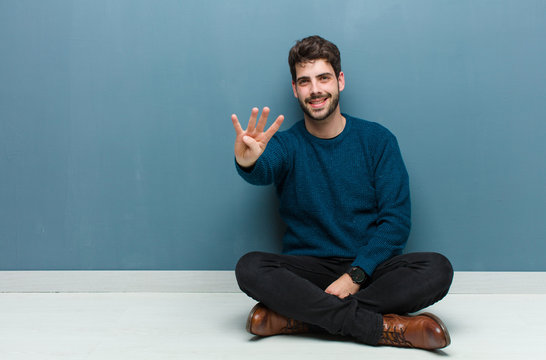 young handsome man sitting on floor smiling and looking friendly, showing number three or third with hand forward, counting down