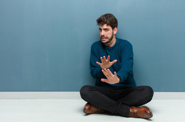young handsome man sitting on floor feeling disgusted and nauseous, backing away from something...