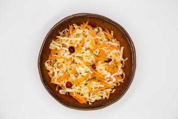 Fresh cabbage salad with carrots and cranberries in a clay bowl on a white background. Raw vegan food concept.
