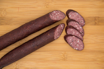 Two deer home sausages with thin slices on a wooden board. Wild meat delicacies for gourmets.