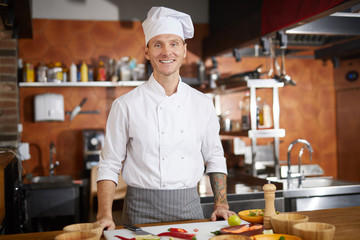 Waist up portrait of handsome chef smiling at camera while standing in restaurant kitchen, copy space