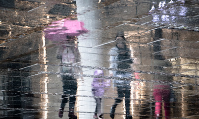 Blurry reflection shadow silhouette of  people and a child walking together under umbrella on a rainy day