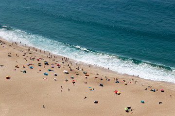 People on the beach  in front of Beautiful crushing wave of Atlantic ocean, captured during the walk along the sandy beach in Nazare, Portugal