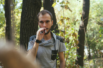 Thin man Smoking a cigarette standing in the woods. Hipster smokes in the Park