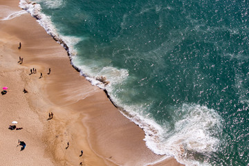 Drone view of people on the yellow sand beach facing the Beautiful crushing waves of Atlantic ocean in Nazare, Portugal