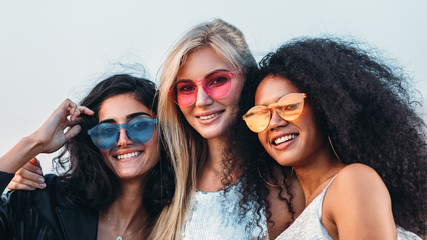 Three happy women wearing sunglasses hugging at evening outdoors