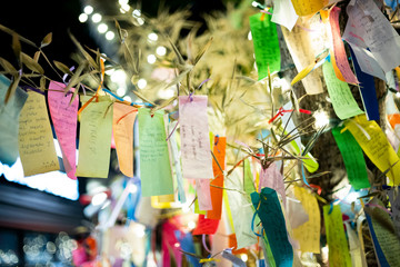 Wishes written on Tanzaku, small pieces of paper, and hung on a Japanese wishing tree, located in the Little Tokyo section of Los Angeles, California, photographed at an outdoor mall at night.  - obrazy, fototapety, plakaty