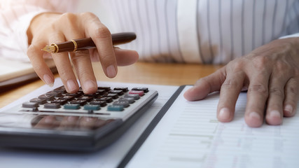 Close-up of businessman hand using calculator to calculate business data, accountancy document at home office.