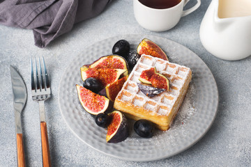 Traditional Belgian waffles with powdered sugar grapes and figs. Cozy homemade Breakfast. Gray concrete background. Copy space.