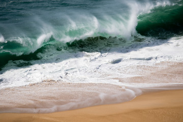 Beautiful crushing wave of Atlantic ocean, captured during the walk along the sandy beach in Nazare, Portugal