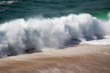 Beautiful crushing wave of Atlantic ocean, captured during the walk along the sandy beach in Nazare, Portugal