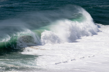 Beautiful crushing wave of Atlantic ocean, captured during the walk along the sandy beach in Nazare, Portugal