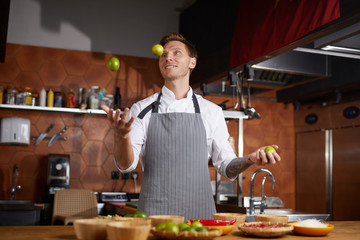 Waist up portrait of handsome professional chef juggling limes while cooking spicy food in Chinese restaurant, copy space