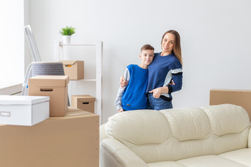 Positive smiling single mother and charming son are posing standing in a new bright comfortable apartment. The concept of moving and mortgages for new housing.