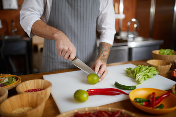 Close up of unrecognizable chef cutting limes and hot pepper while cooking spicy Asian food in restaurant kitchen, copy space