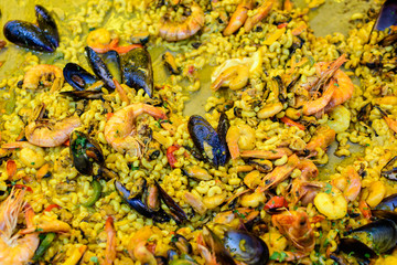 Close up of large portion of traditional Spanish paella dish freshly being cooked with seafood and pasta in a  frying pan at a street food festival, ready to eat seafood, side view, selective focus