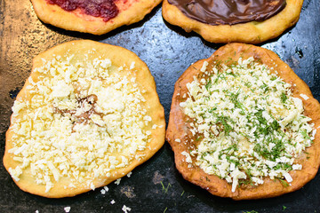 Close up of a langos, typical Hungarian food specialty, with white cheese and dill on an iron sheet, deep fried dough in direct sunlight, available for sale at a street food market 
