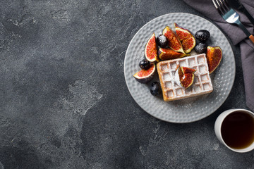 Traditional Belgian waffles with powdered sugar grapes and figs. Cozy homemade Breakfast. Gray concrete background. Copy space.