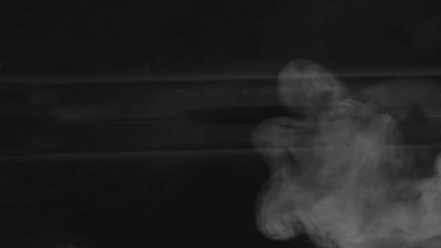 Realistic abstract smoke vapor spreads from the right side with glares. White smoke in slow motion on black background. Floating fog cloud over black background through the space.